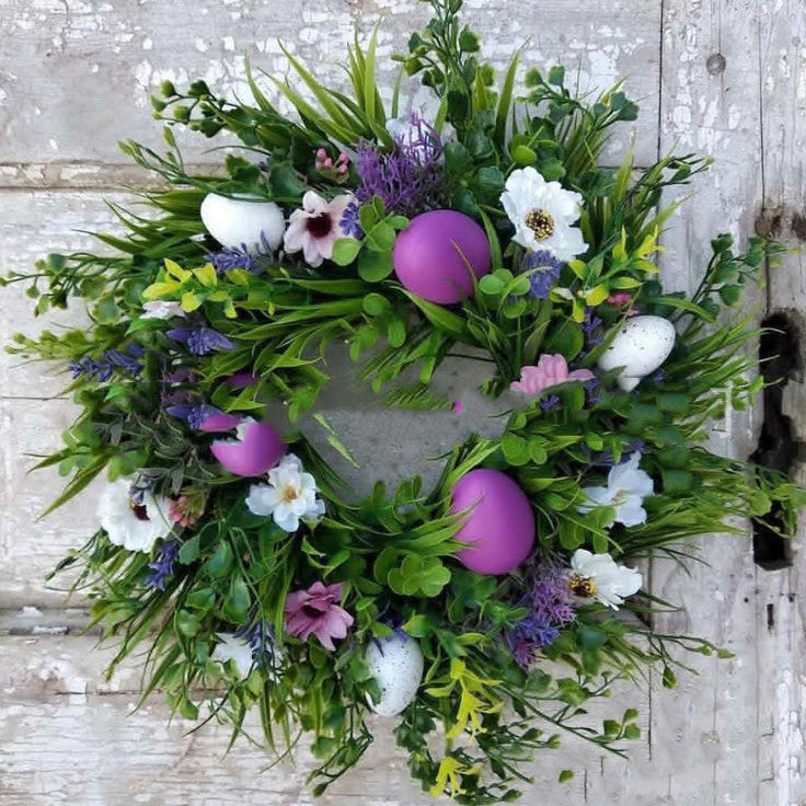 Wreath with greenery, flowers, and Easter eggs on a wooden background