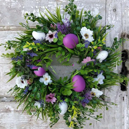 Wreath with greenery, flowers, and Easter eggs on a wooden background