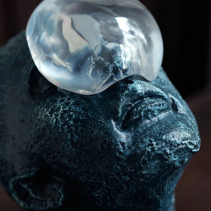 Close-up of a textured blue sculpture with a clear glass orb on top against a dark background